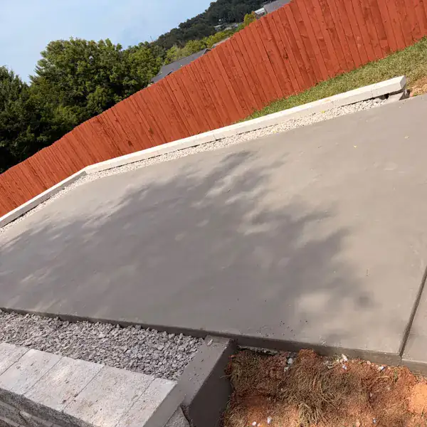 Concrete patio edge and step beside a wooden fence